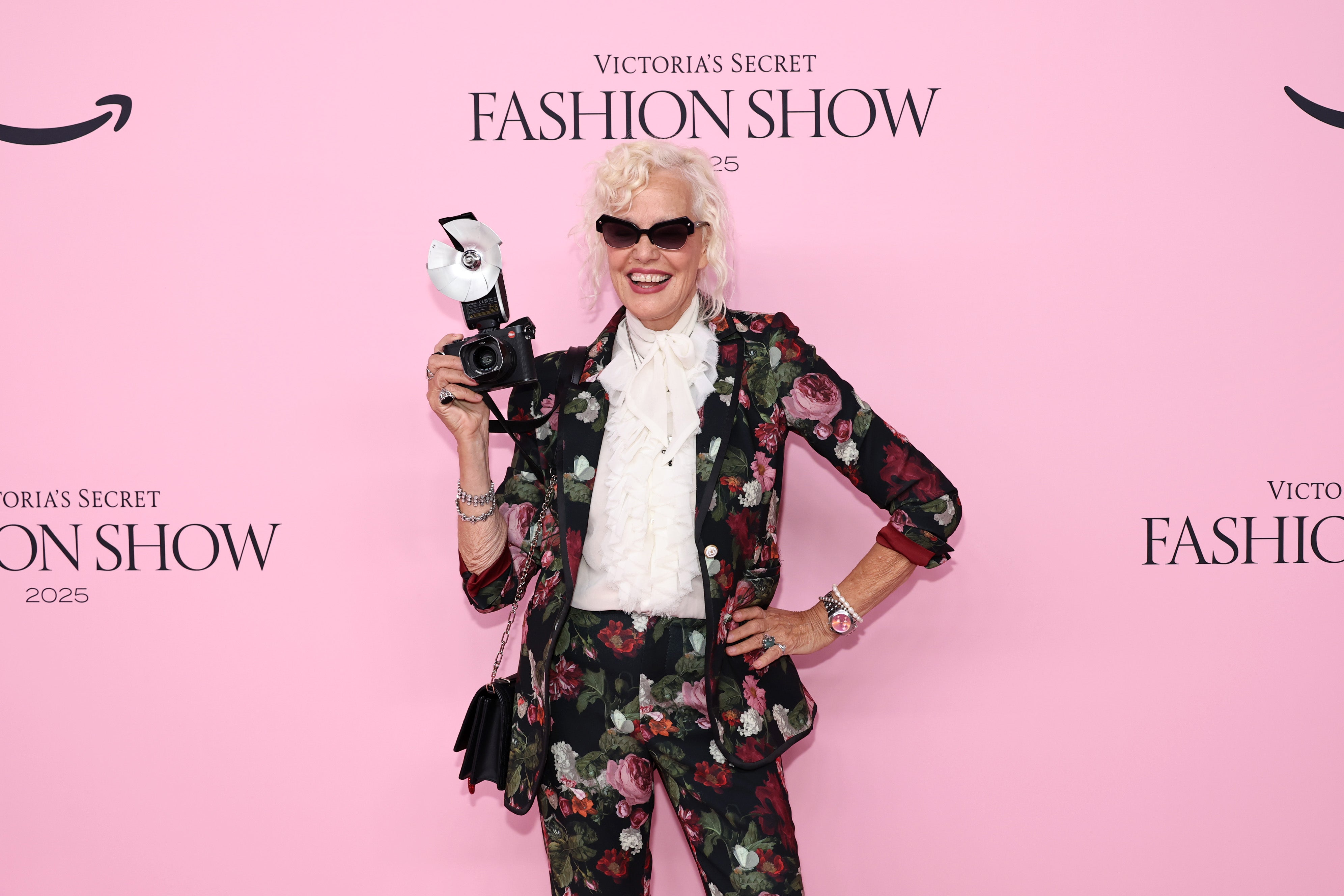 German photographer Ellen von Unwerth sported a floral pantsuit for the occasion, accessorized by a white top tied in a bow at the neck, sunglasses, an over-the-shoulder bag, and a camera