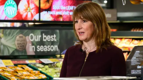 PA Media Rachel Reeves stands in front of the fruit aisle in a Tesco supermarket wearing a red zip-up top