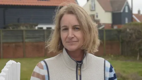 Jamie Niblock/BBC Teresa Lane smiles at the camera from her garden. She has short blonde hair and wears a wool fleece jacket.