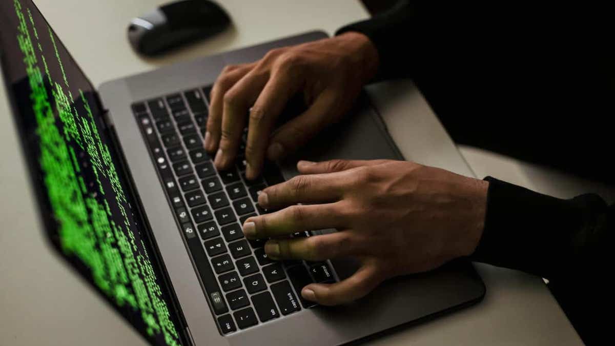 Hands typing on a laptop with green code on screen