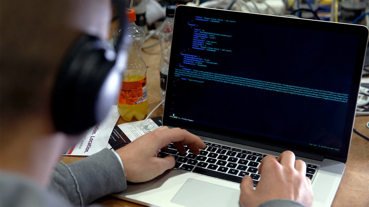 A man uses a laptop with code on the screen.